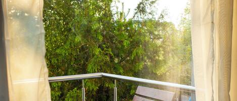 A balcony with a wooden bench, metal railings, and a view of greenery.