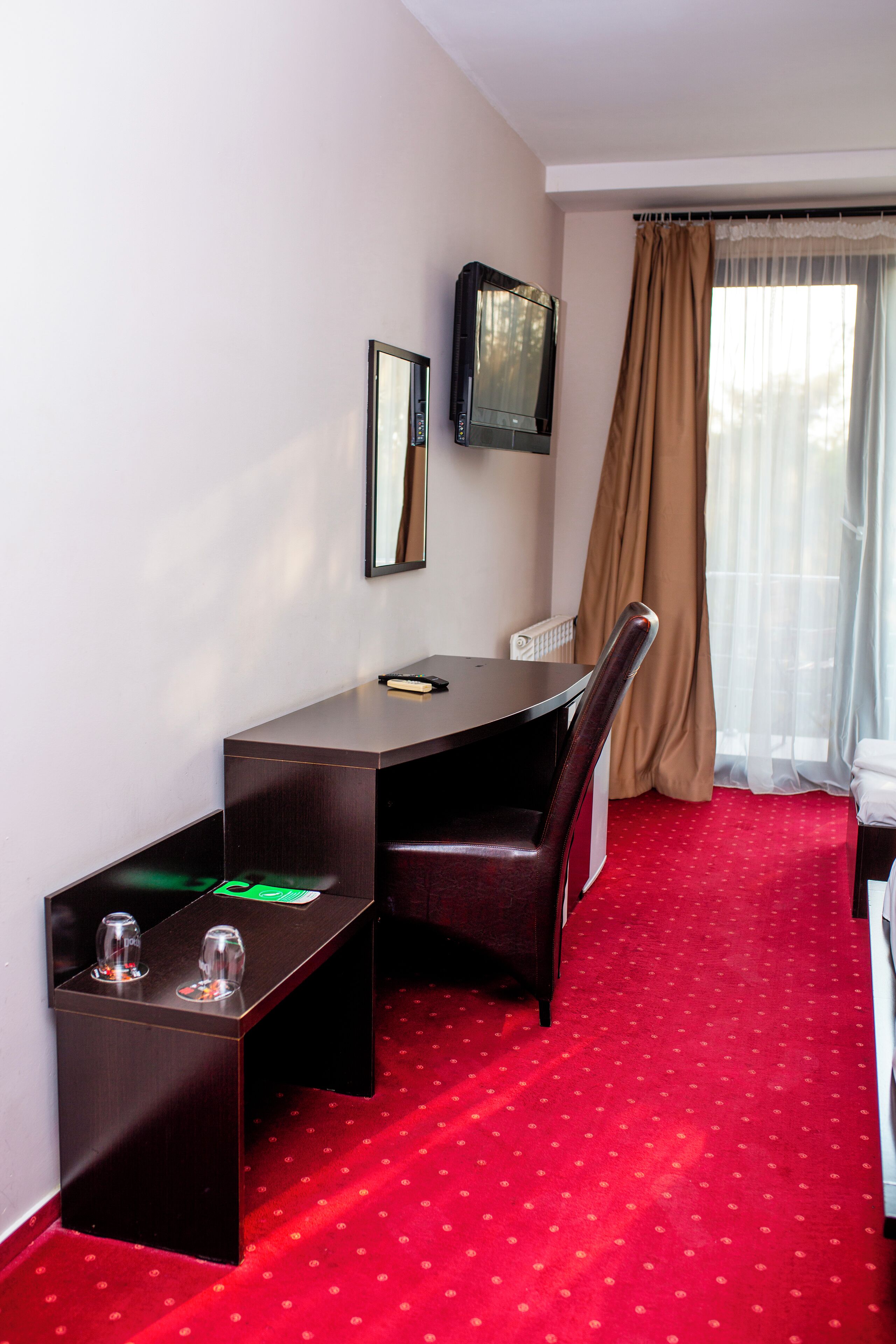 A hotel room with a desk, chair, and a television mounted on the wall.