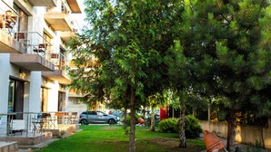 Um edifício residencial com varandas, uma área gramada com árvores e um carro estacionado.