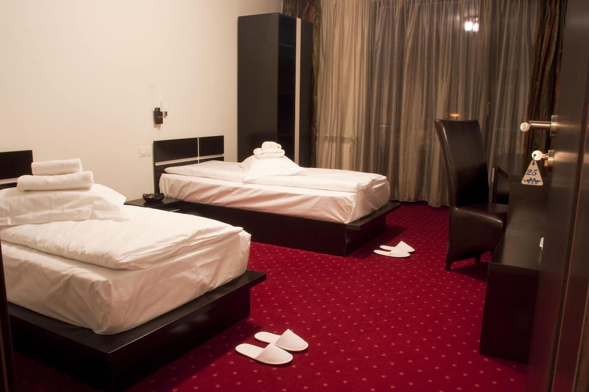 A hotel room with two beds, a red carpet, a desk, and a chair.