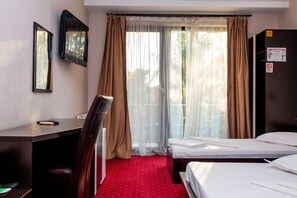 A hotel room with a desk, two beds, a chair, a radiator, and a window with curtains.