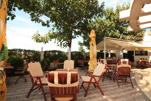 An outdoor seating area with wooden chairs and tables, a large umbrella, and a building with a sign that reads 'restaurant' in the background.