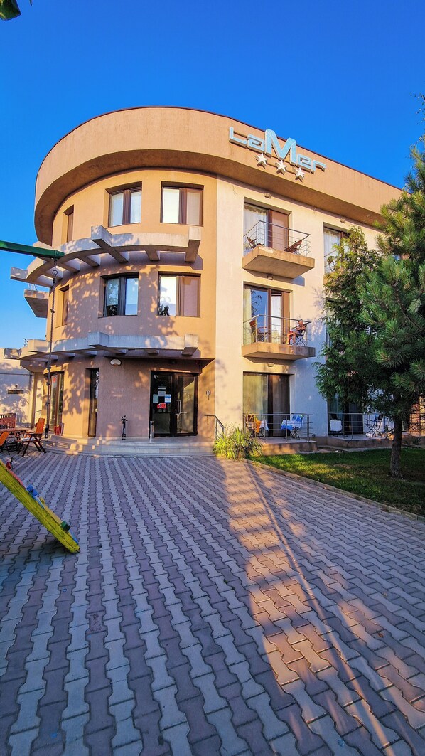 A modern building with a curved facade, multiple balconies, and a paved entrance area.