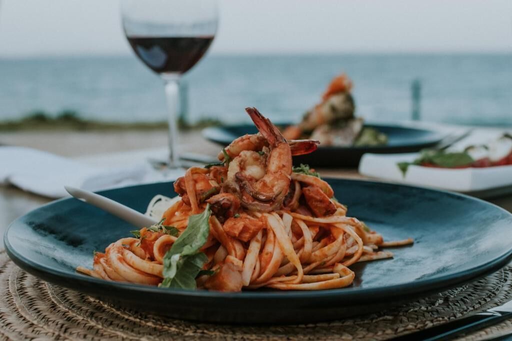 A seafood pasta dish on a plate with a glass of red wine in the background.