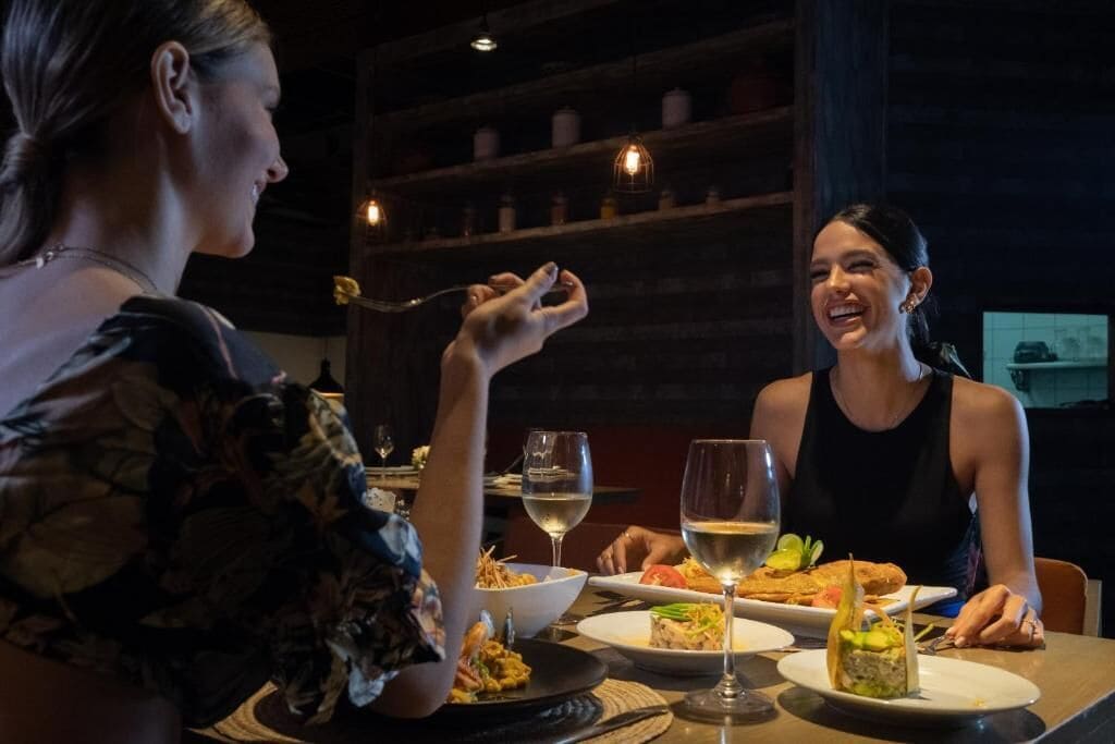 Dos personas cenando en un restaurante con ambiente oscuro y estanterías al fondo.