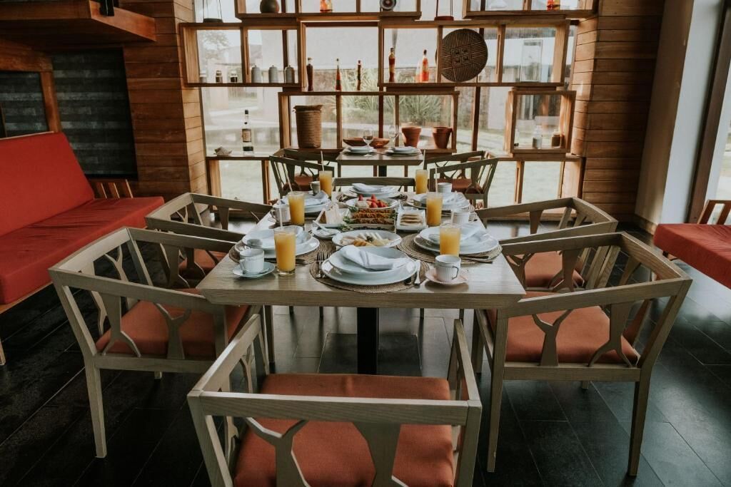 A dining area with a wooden table set for four, surrounded by chairs with orange cushions.