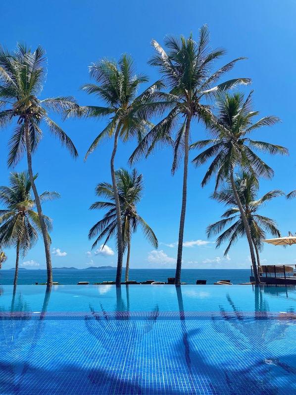 Zona de piscina con palmeras y vista al océano.