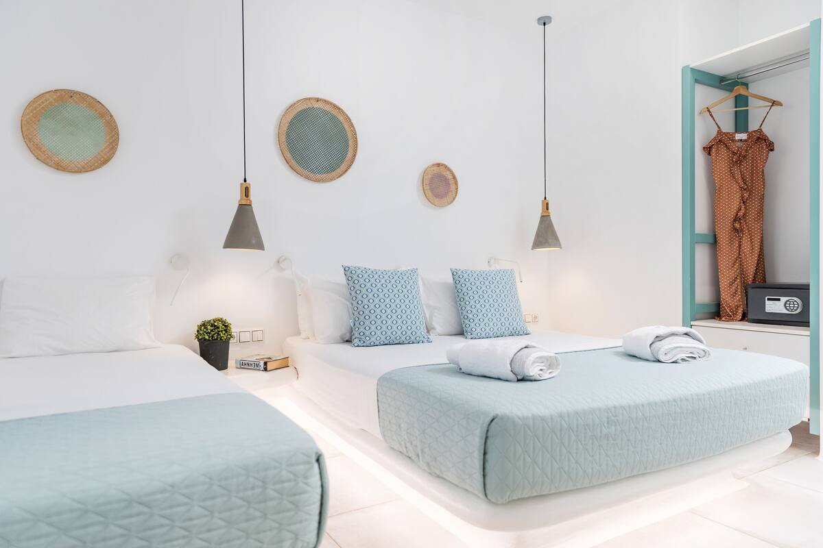 A modern hotel room with two beds, a small plant, a clock, and a hanging dress on a rack.