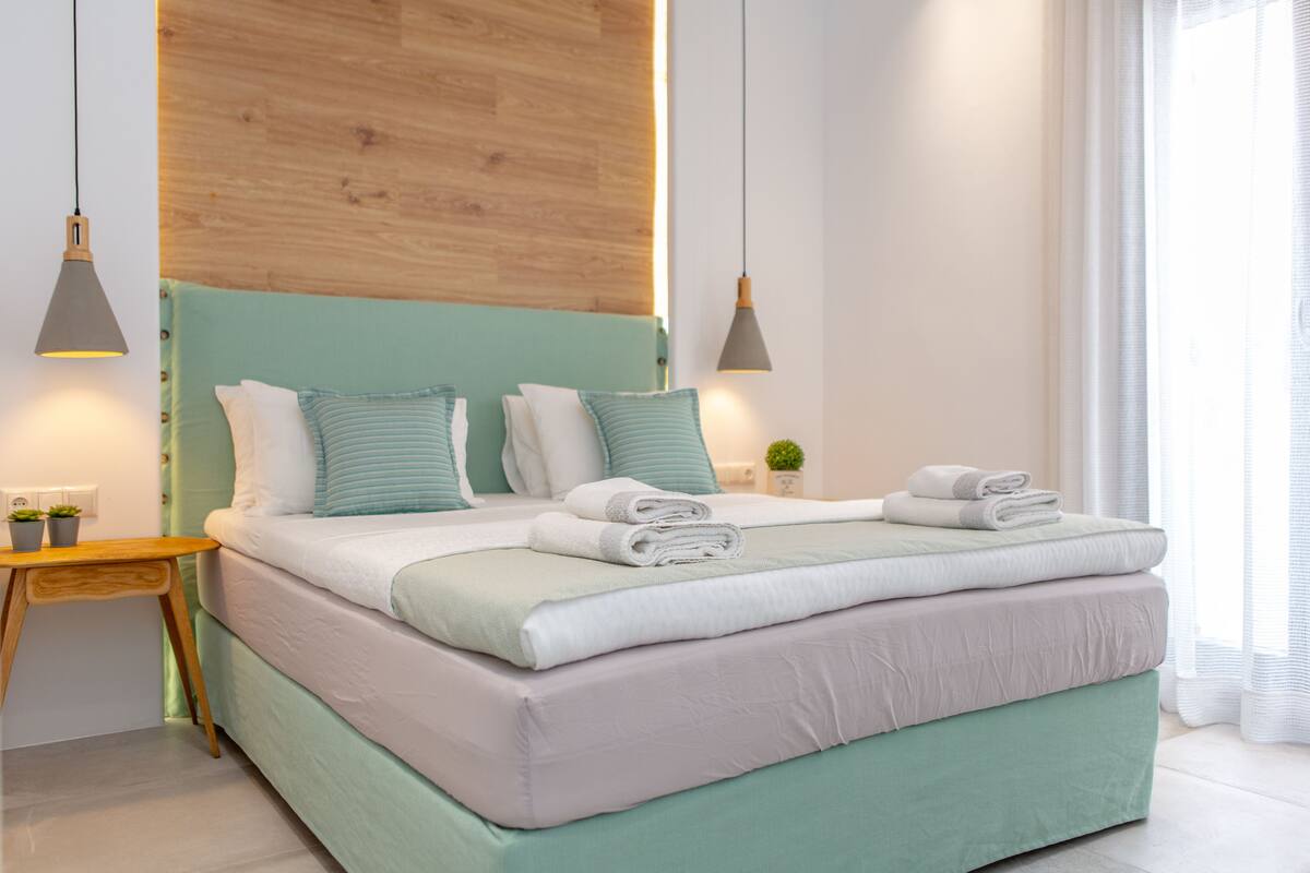 A modern bedroom with a large bed, wooden headboard, bedside tables, and a small potted plant.