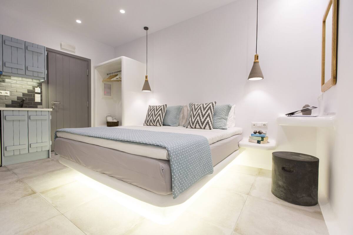 A modern bedroom with a bed, bedside tables, and a built-in kitchen area.