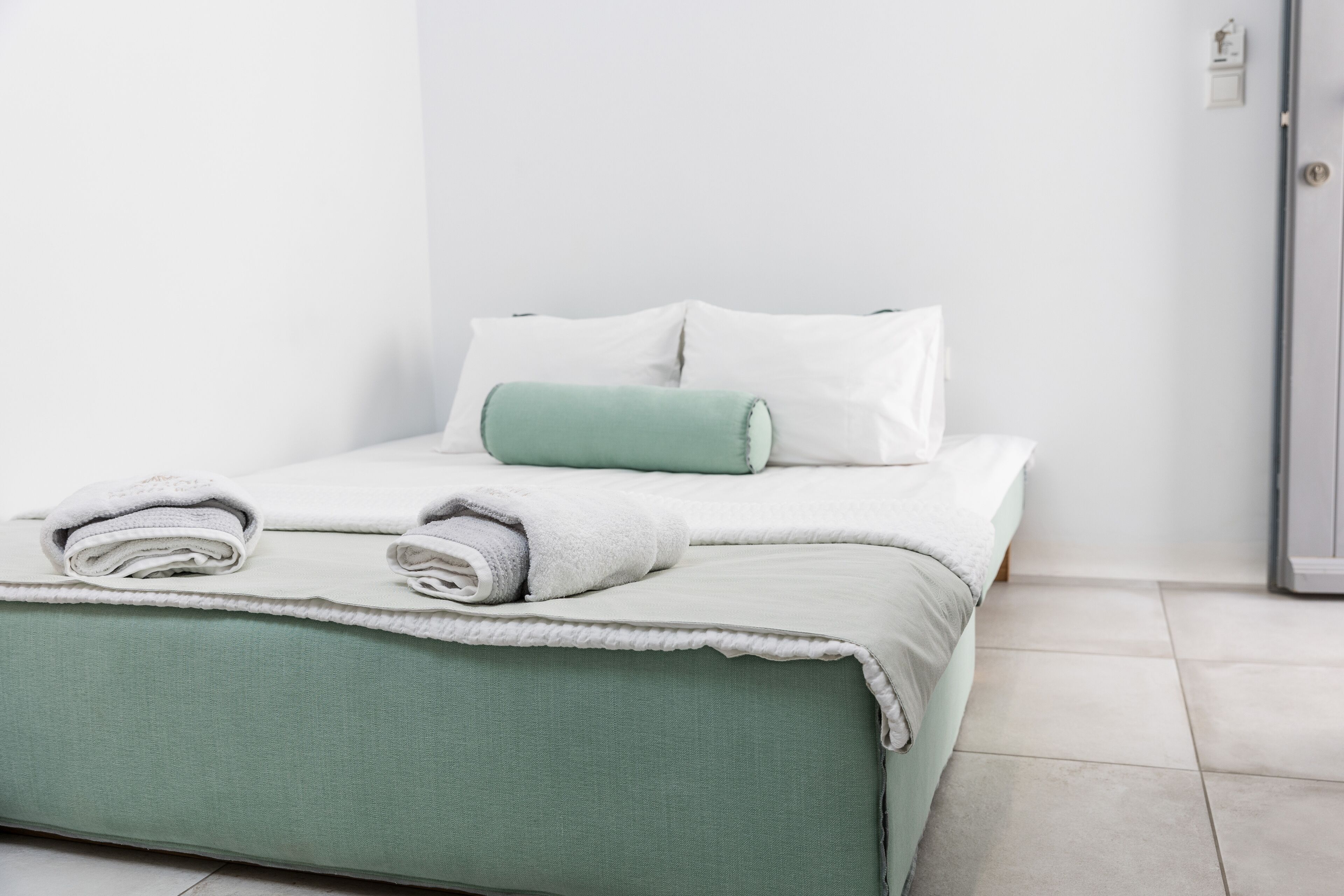 A neatly made bed with a green bedspread, white pillows, and rolled towels.