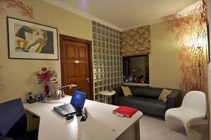 Una sala de estar con un escritorio, una computadora portátil, un sofá y una ventana.