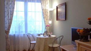 Un comedor con una mesa preparada para dos personas, un televisor y un frutero sobre un mueble de madera.