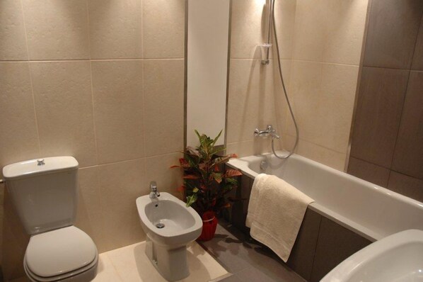 A bathroom with a toilet, bidet, bathtub, and a potted plant.