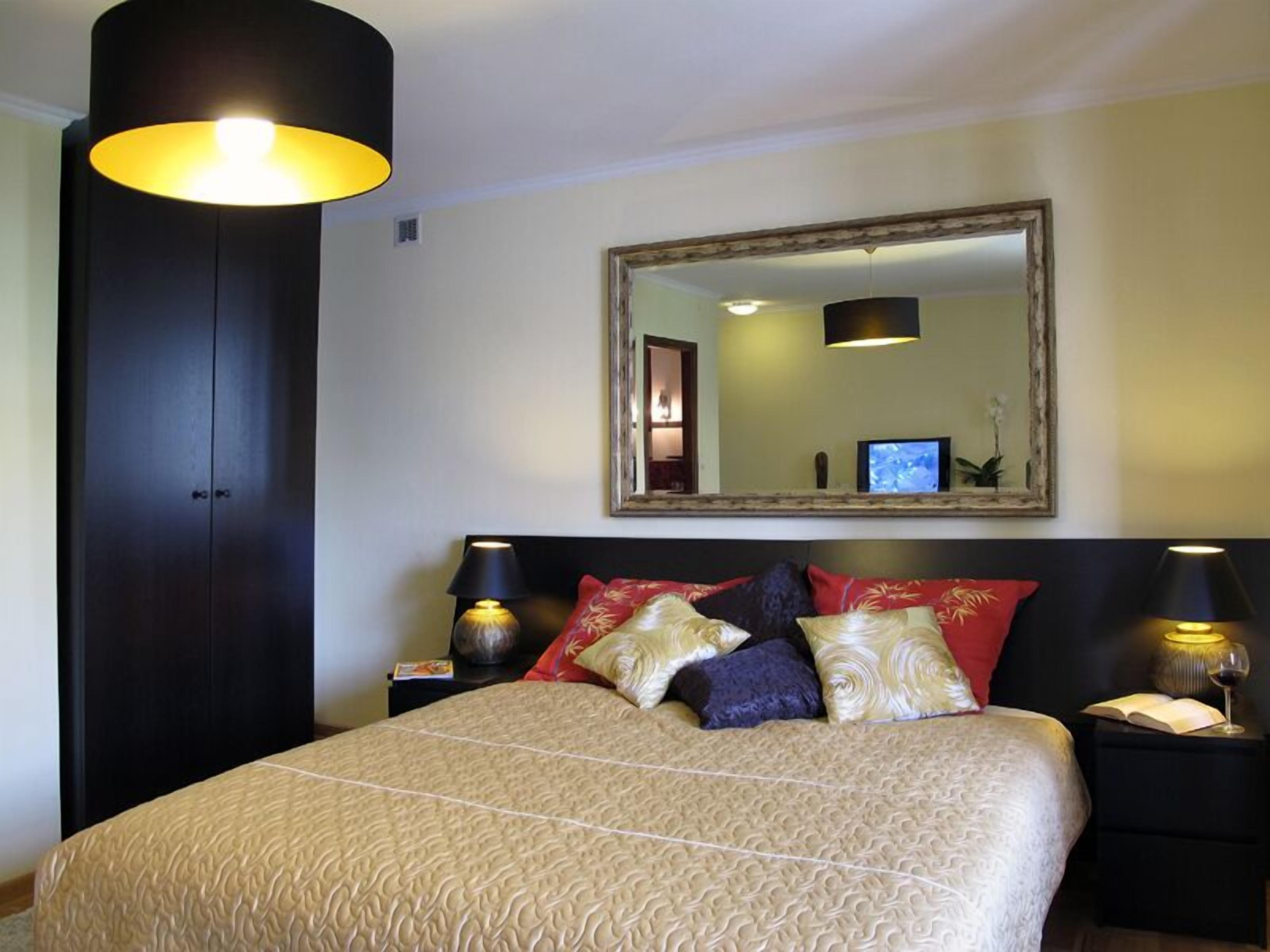 A hotel room with a bed, two bedside tables, a large mirror, and a wardrobe.