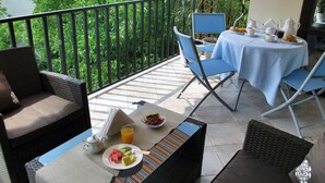 Un balcón con una mesa para desayunar, un sofá de mimbre y una silla.