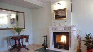 Una habitación con chimenea, un espejo, una mesa con flores y un cuadro en la pared.