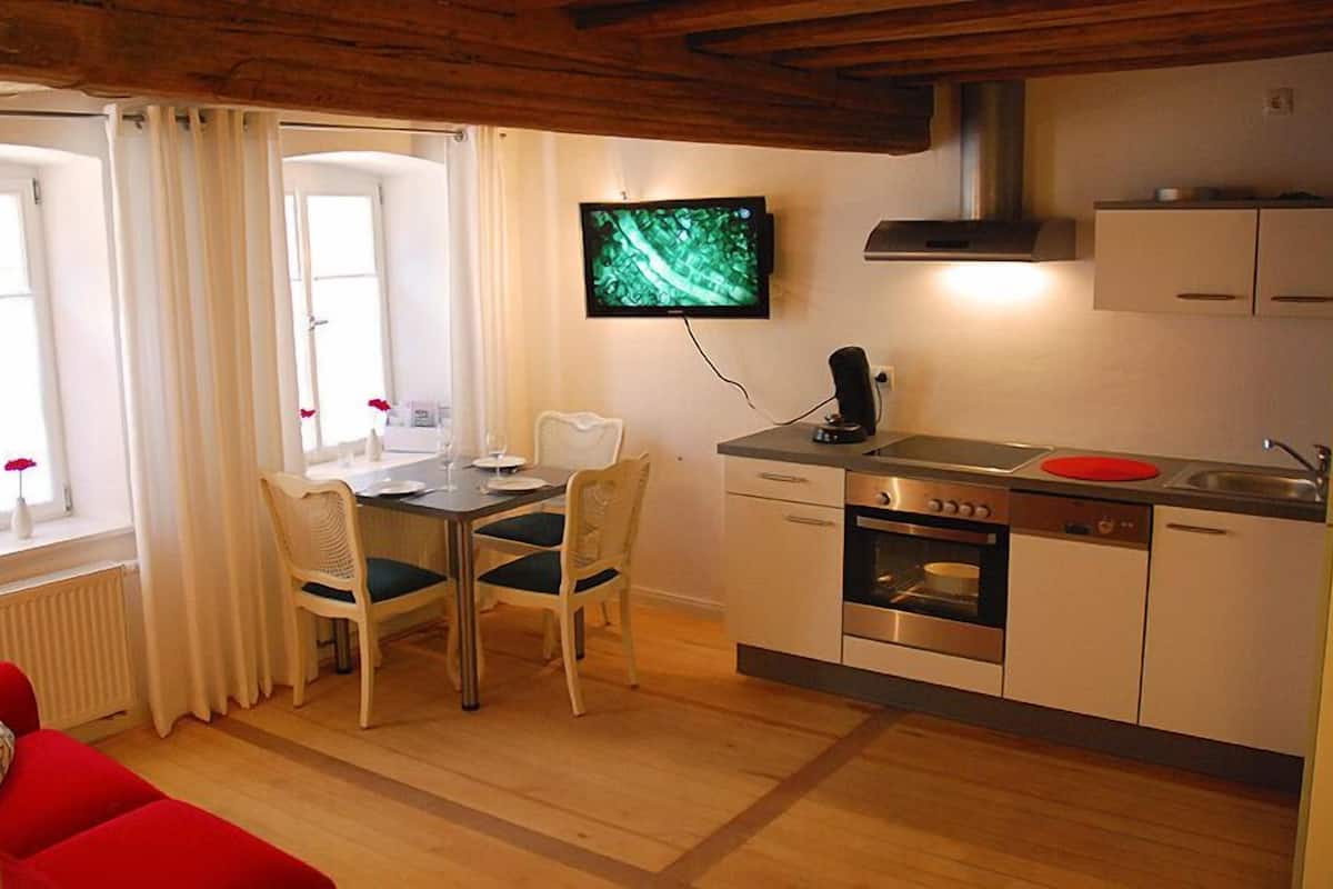Eine kompakte Küche mit Essbereich, einem an der Wand befestigten Fernseher und einem roten Sessel im Vordergrund.