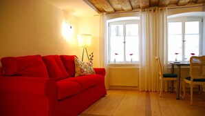 A red sofa, a table with chairs, and a window with curtains. - Ferienwohnung am Rathaus Bamberg (Bamberg)