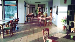A spacious indoor dining area with multiple wooden tables and chairs, large windows, and a tiled floor. - Hotel Villa de Setenil (Setenil de las Bodegas)