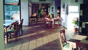 A spacious indoor area with multiple dining tables and chairs, large windows allowing natural light, and a view of the outdoors. - Hotel Villa de Setenil (Setenil de las Bodegas)