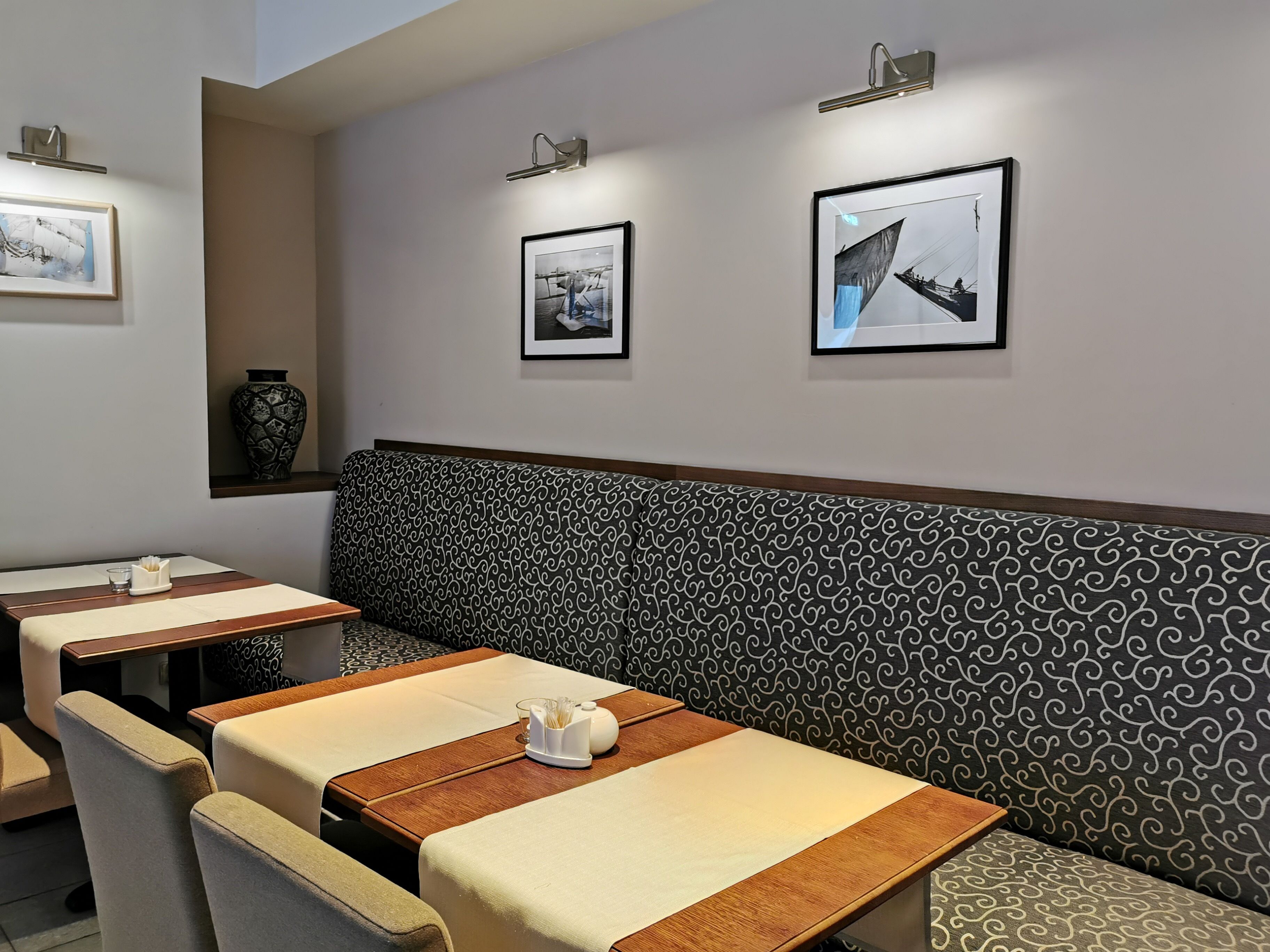 A restaurant interior with a patterned bench, tables with white tablecloths, and framed pictures on the wall.