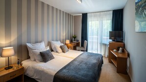 Habitación de hotel con dos camas, un escritorio con televisor, una silla, una lámpara y un cuadro en la pared.
