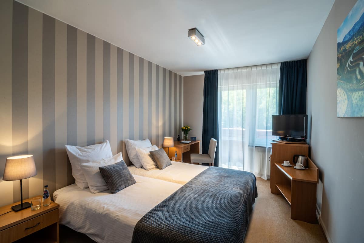 A hotel room with two beds, a desk with a TV, a chair, a lamp, and a painting on the wall.