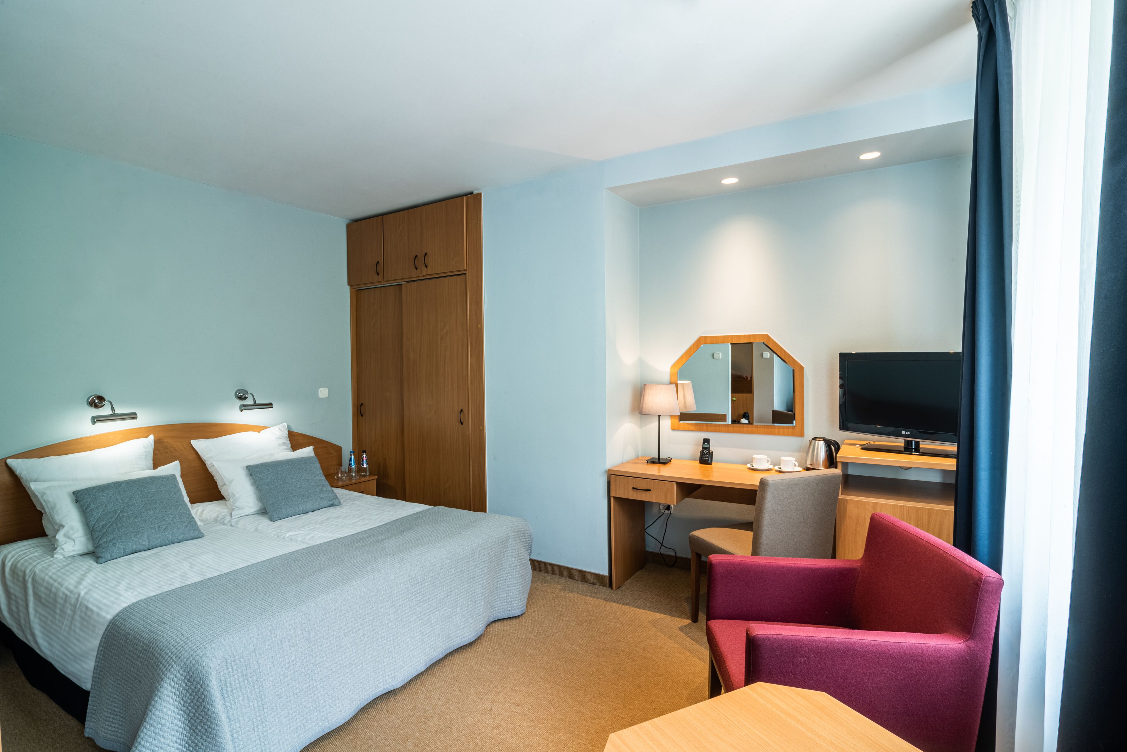 A hotel room with a bed, desk, chair, TV, and wardrobe.