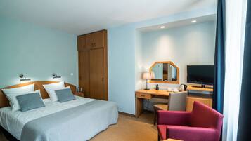 A hotel room with a bed, desk, chair, TV, and wardrobe.