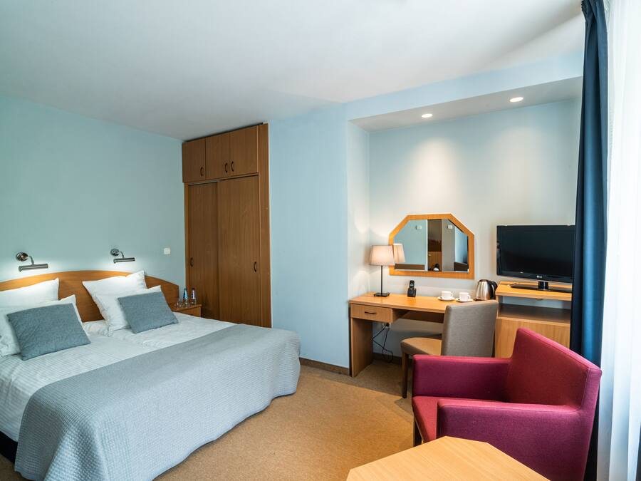 A hotel room with a bed, desk, chair, TV, and wardrobe.