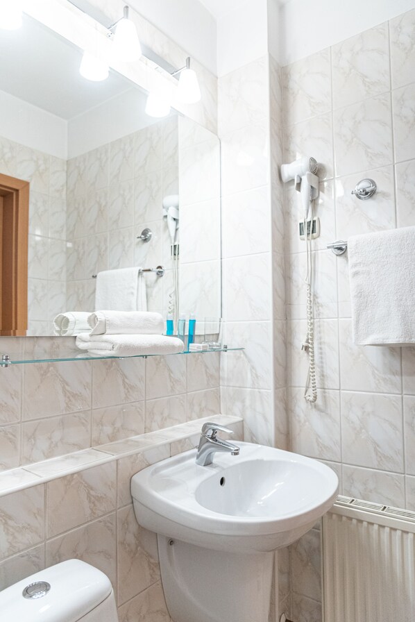 Un baño moderno con pared de azulejos de mármol, repisa de vidrio con artículos de aseo, lavabo blanco y un inodoro.