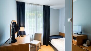 Een hotelkamer met een bed, een bureau met een computer, een stoel, een televisie en een koffiezetapparaat.