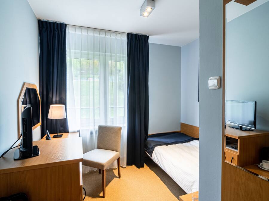 Een hotelkamer met een bed, een bureau met een computer, een stoel, een televisie en een koffiezetapparaat.