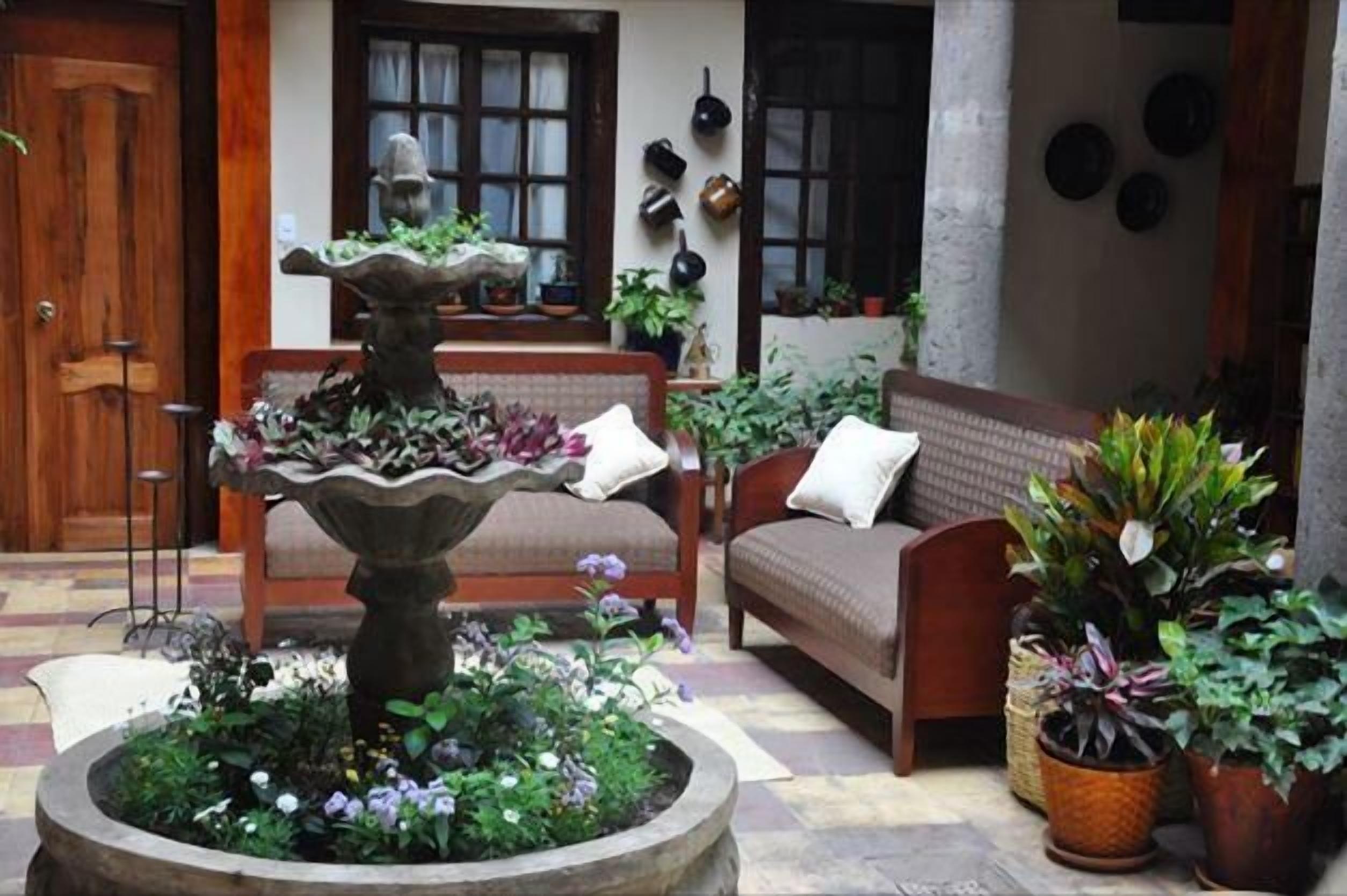 A cozy courtyard with a stone fountain, a wooden bench, and a sofa with cushions.