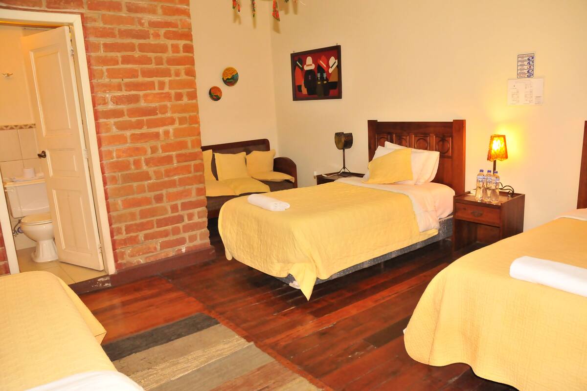 Une chambre d’hôtel avec deux lits, un mur en briques, un plancher en bois, une table de chevet avec une lampe et un tableau accroché au mur.