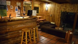 Een rustiek houten interieur met een bar, houten krukken, een bank en een grote koperen pot.