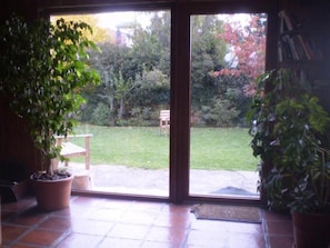 Ein Zimmer mit einer Schiebetür aus Glas, die in einen Garten führt. In der Nähe der Tür befindet sich eine hölzerne Bank und ein Blumentopf.