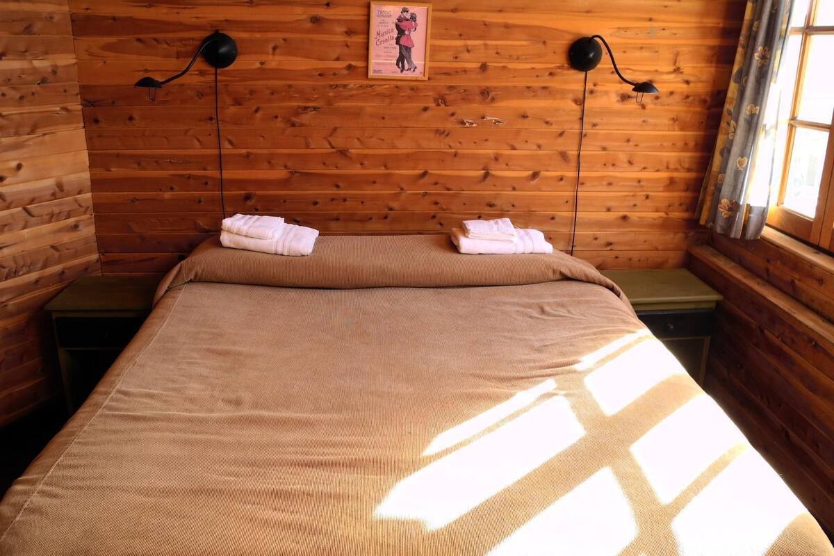 Een kamer met houten lambrisering, een bed, twee bedlampen en een raam met gordijnen.