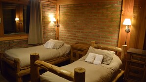 Twee houten bedden met hoofdborden, een bakstenen muur en twee bedlampen.