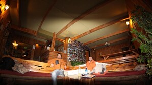 Een rustiek houten interieur met een zithoek met een houten bank, een wand vol foto's en een kleine tafel met een fles en een boek.