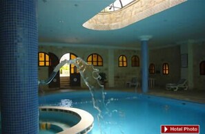 An indoor swimming pool with clear water, a central fountain, and arched windows in the background. - Amra Palace International Hotel (Wadi Musa)