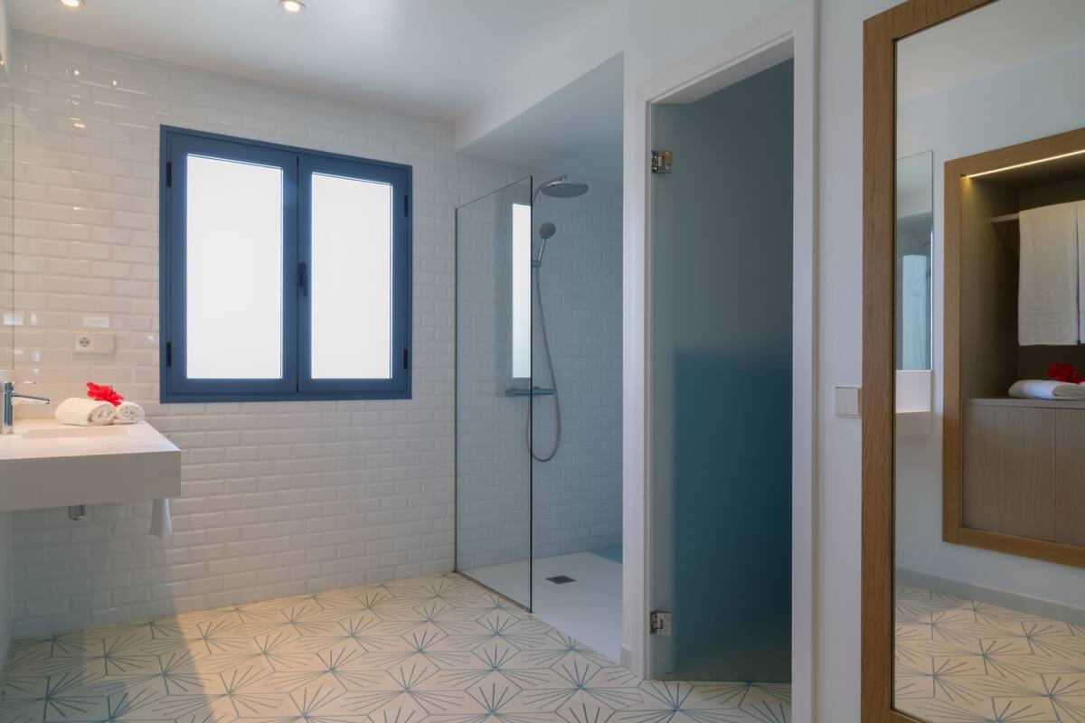 A modern bathroom with a glass-enclosed shower, a white sink with a towel, and a window.