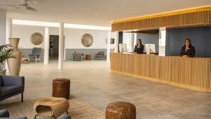 A modern reception area with a wooden reception desk, two receptionists, and a seating area with a large vase and a wicker chair. - Oasis Lanz Beach Mate (Teguise)