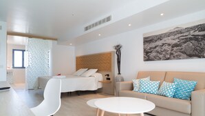 A modern hotel room with a bed, a sofa, a dining table, and a large wall art piece. - Oasis Lanz Beach Mate (Teguise)