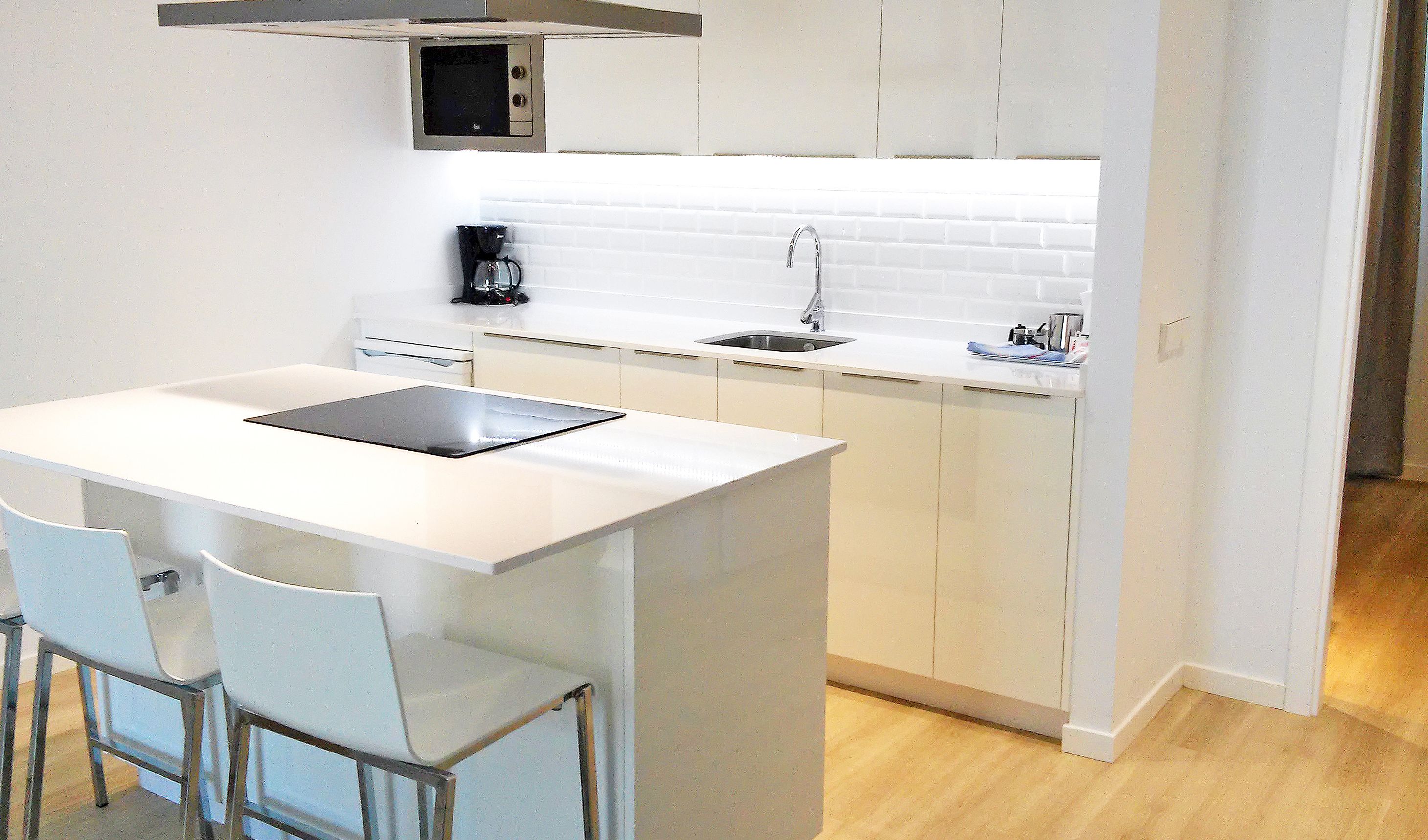 Una cocina compacta con encimera blanca, cafetera y lavamanos.