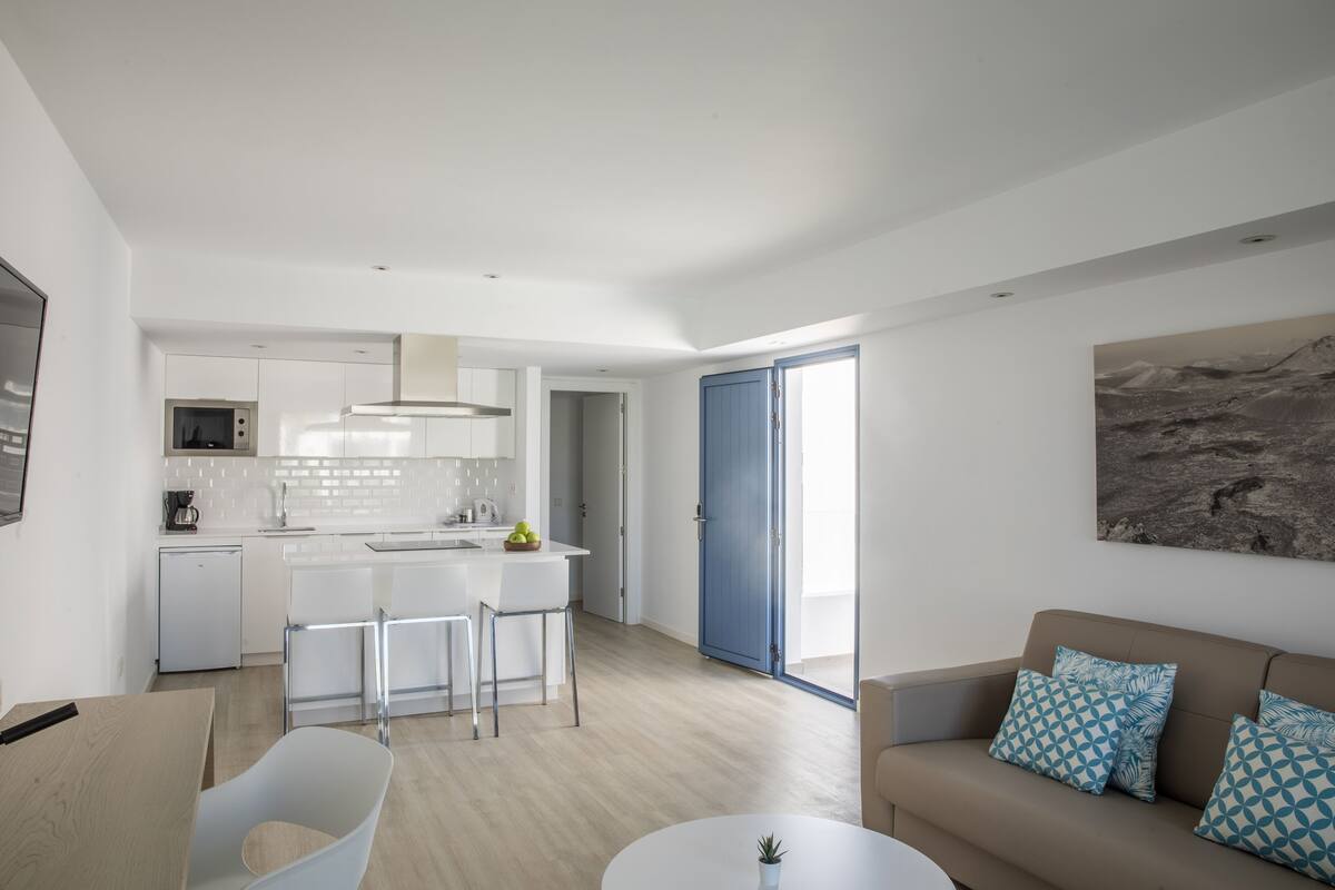 A modern kitchen with white cabinets, a central island, and a dining area with a white table and chairs.