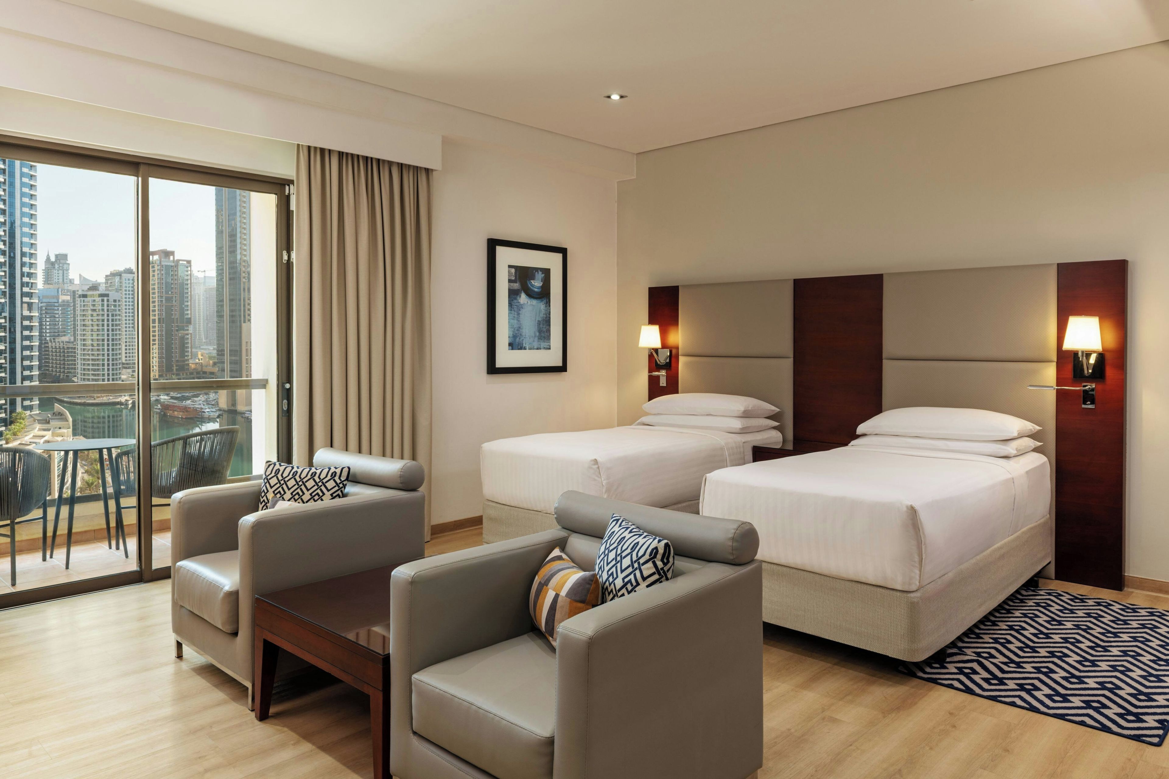A hotel room with a city view, two beds, a sofa, and a dining area with a table and chairs.