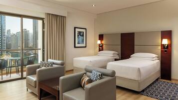 A hotel room with a city view, two beds, a sofa, and a dining area with a table and chairs.