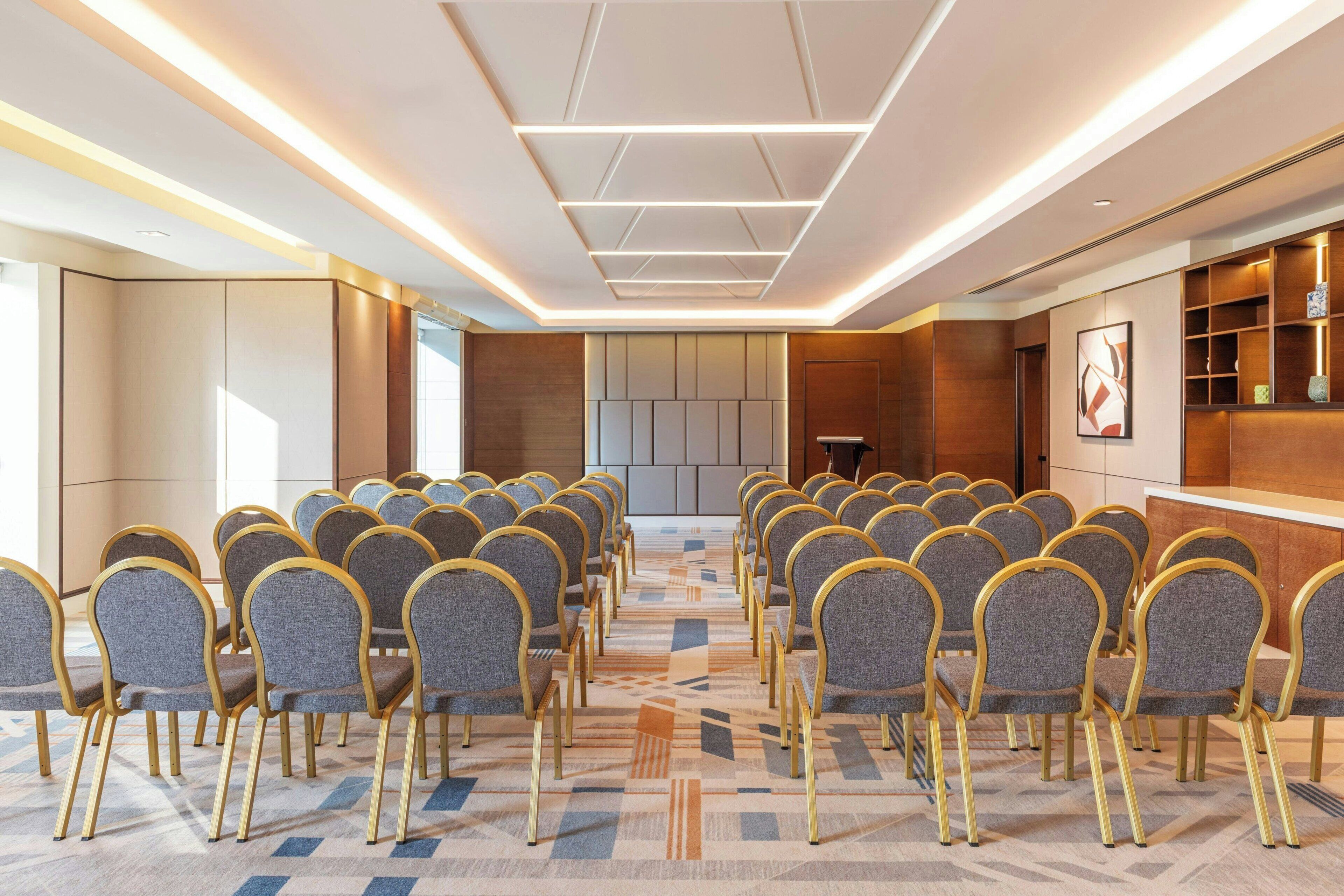 Une salle de conférence avec des rangées de chaises, un pupitre et un design moderne au niveau du plafond.